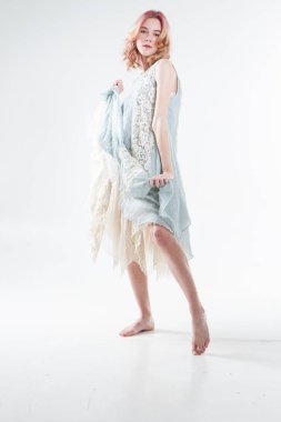 Barefoot blonde in a long dress. Studio portrait on a white background.