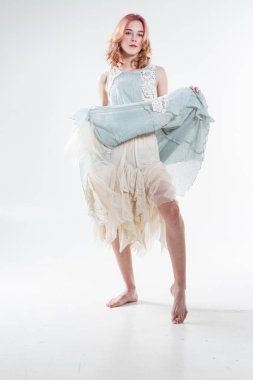 Barefoot blonde in a long dress. Studio portrait on a white background.