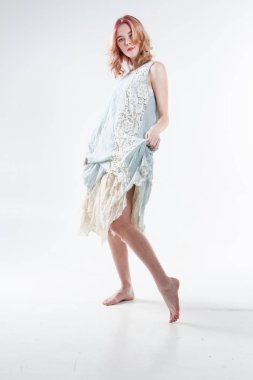Barefoot blonde in a long dress. Studio portrait on a white background.