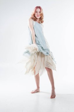 Barefoot blonde in a long dress. Studio portrait on a white background.
