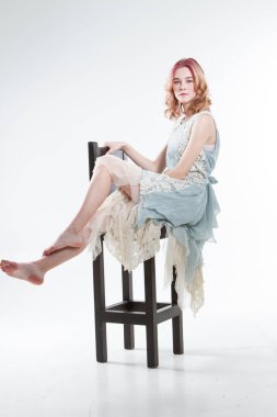 Genç kız yüksek bir bar taburesinde oturuyor. Beyaz arkaplanda stüdyo portresi