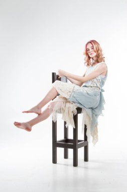 Genç kız yüksek bir bar taburesinde oturuyor. Beyaz arkaplanda stüdyo portresi
