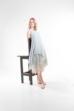 Genç kız yüksek bir bar taburesinin yanında duruyor. Beyaz arkaplanda stüdyo portresi