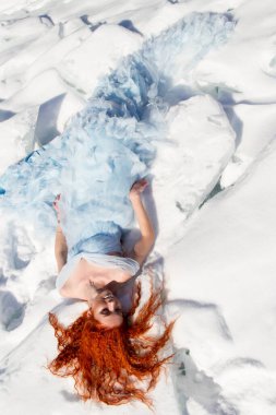 Gece elbisesi içindeki genç kız karda yatıyor.