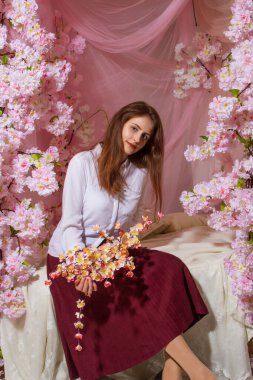 Genç kız yatak odasında çiçeklerle süslenmiş bir yatakta oturuyor.