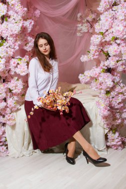 Genç kız yatak odasında çiçeklerle süslenmiş bir yatakta oturuyor.