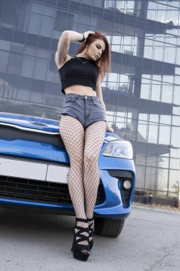 Bir araba ve ofis binasının arka planında uzun bacaklı genç bir kız.