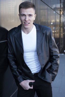 Deri ceketli bir adam bir ofis binasının arka planında.