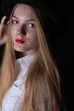 Siyah şapkalı sarışın ve karanlık bir odada beyaz gömlekli..