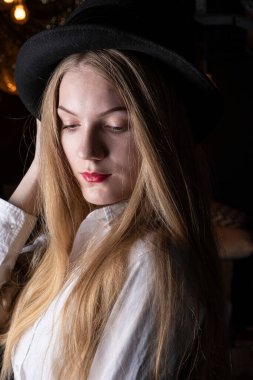 Siyah şapkalı sarışın ve karanlık bir odada beyaz gömlekli..