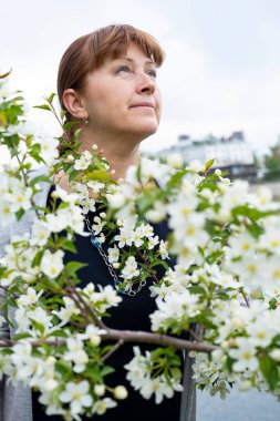 Yaşlı bir kadın çiçek açan bir elma ağacında sevinir.