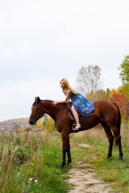 Sonbahar ormanında at süren açık renk bir yaz elbisesi içindeki sarışın.