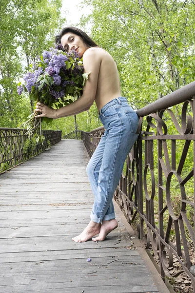 裸の少女が歩道橋の上に立ってライラックの花束を持っています — ストック写真