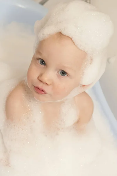 The boy bathes in a bath with foam