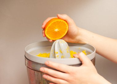 Portakal suyu tutan kadın eller ve taze sıkılmış narenciye suyu sıkacağı yardımıyla taze sıkılmış turunçgil meyvesi yapıyorlar.