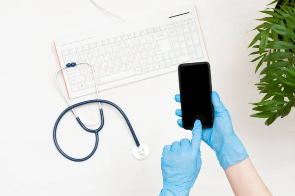 Mavi eldivenli doktor dokunmatik ekranlı telefonu elinde tutuyor. Doktorun çalışma yeri..