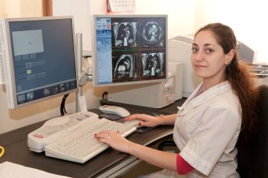 Ekranda röntgen filmleri olan bir kadın doktor masada oturuyor. CAT taraması.