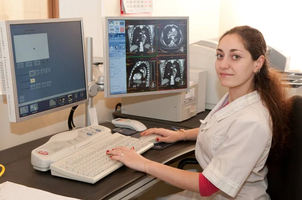 Ekranda röntgen filmleri olan bir kadın doktor masada oturuyor. CAT taraması.