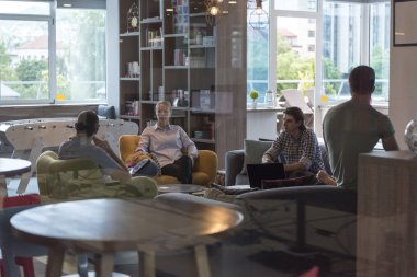 Modern ofisteki gençler, laptopta çalışırken ve kahve içerken takım toplantısı ve beyin fırtınası yapıyorlar.