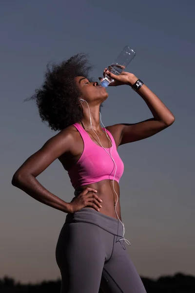 Mujer afroamericana bebiendo agua después de correr en la naturaleza — Foto de Stock