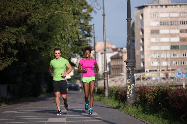 Mladý, usměvavý mnohonárodnostní pár běhání ve městě — Stock fotografie