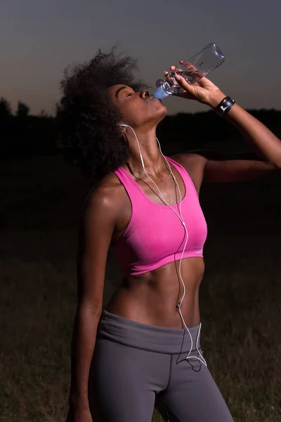 Mulher afro-americana bebendo água depois de correr na natureza — Fotografia de Stock