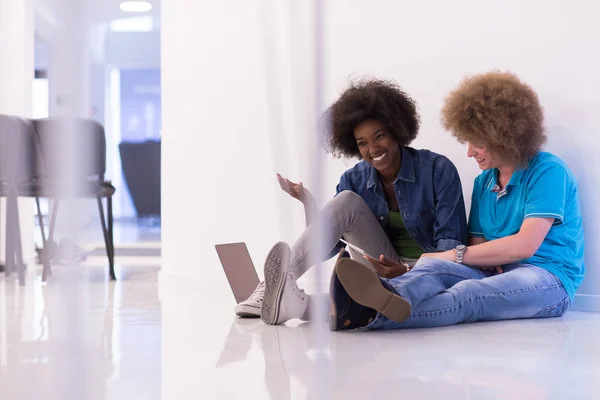 Multi-etnisch paar zittend op de vloer met een laptop en tablet — Stockfoto