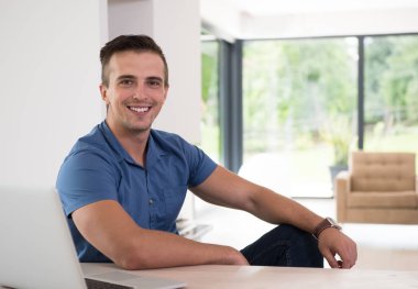 Evde dizüstü bilgisayarı olan genç bir adam.