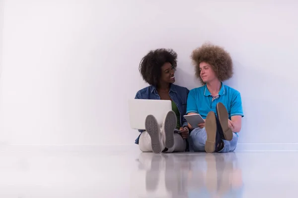 Coppia multietnica seduta sul pavimento con un computer portatile e tablet — Foto Stock