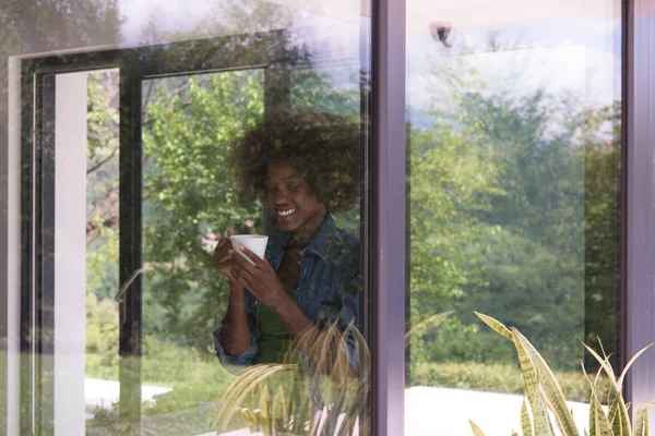 Mujer afroamericana bebiendo café mirando por la ventana —  Fotos de Stock