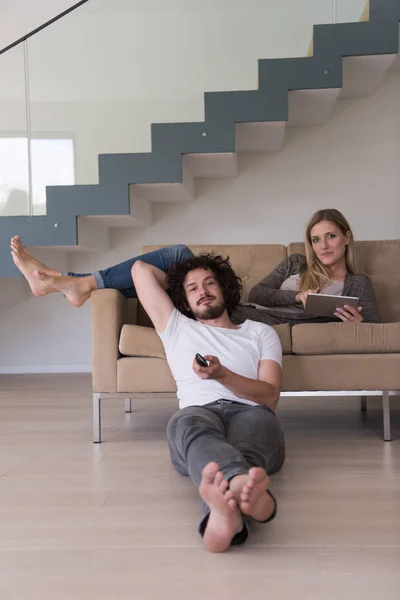 若いカップルがタブレットとリモート コントロールを使用して 豪華なリビング ルームのソファに緩和します — ストック写真