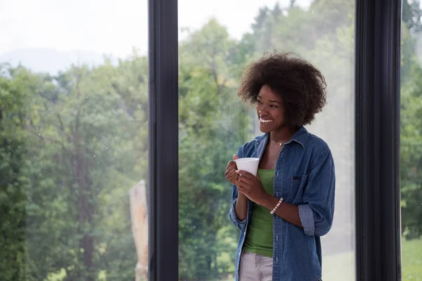 Donna afroamericana che beve caffè guardando fuori dalla finestra — Foto Stock