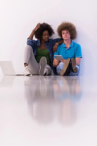 Couple multiethnique assis sur le sol avec un ordinateur portable et tablette — Photo