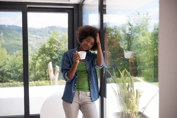 Donna afroamericana che beve caffè guardando fuori dalla finestra — Foto Stock