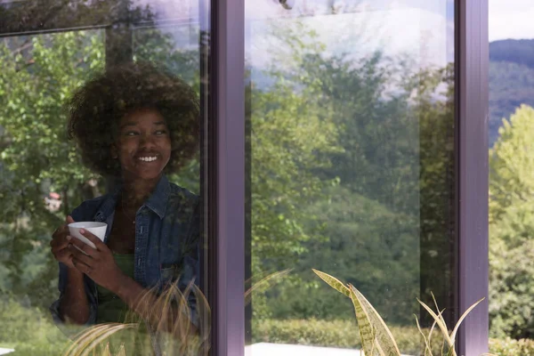 African American vrouw drinken koffie kijkt uit het raam — Stockfoto