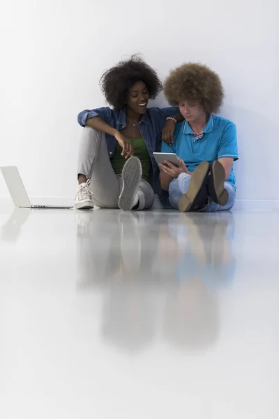 Багатоетнічна пара сидить на підлозі з ноутбуком і планшетом — стокове фото