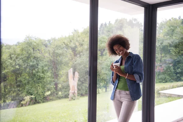 African American woman dricka kaffe tittar ut genom fönstret — Stockfoto