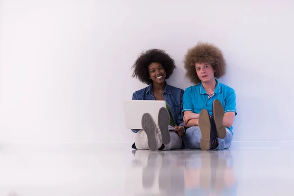 Multi-etnisch paar zittend op de vloer met een laptop en tablet — Stockfoto