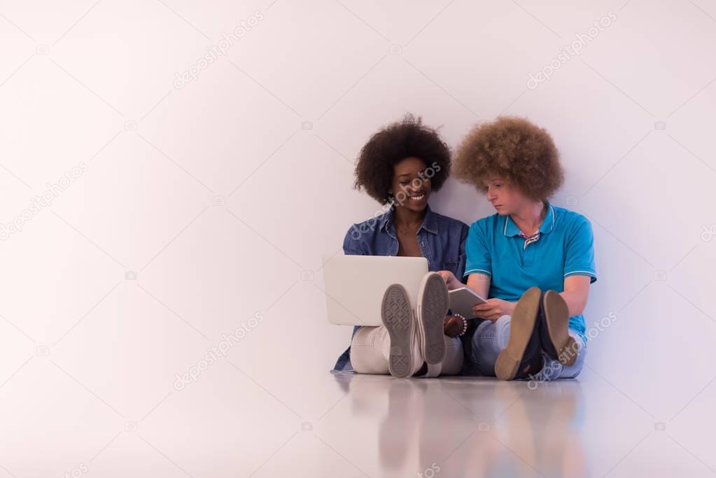 multiethnic couple sitting on the floor with a laptop and tablet
