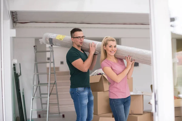 Casal carregando um tapete se mudando para casa nova — Fotografia de Stock