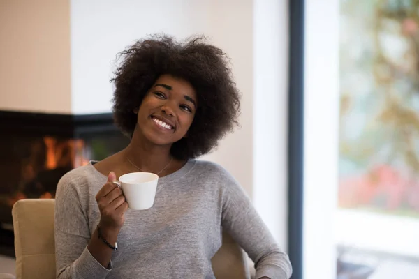 Zwarte vrouw drinken koffie voor open haard — Stockfoto