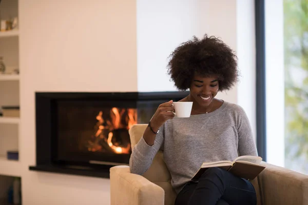 Black woman reading book  in front of fireplace — Stock Photo, Image