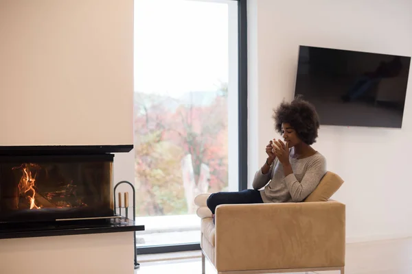 Mujer negra bebiendo café frente a la chimenea — Foto de Stock