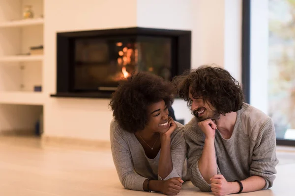 Pareja multiétnica tumbada en el suelo frente a la chimenea —  Fotos de Stock