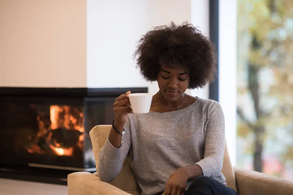 Zwarte vrouw drinken koffie voor open haard — Stockfoto