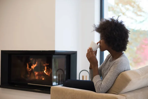 暖炉の前でコーヒーを飲みながら黒人の女性 — ストック写真