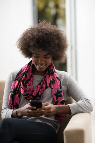 Mujer negra sentada en el sofá y usando el teléfono móvil —  Fotos de Stock