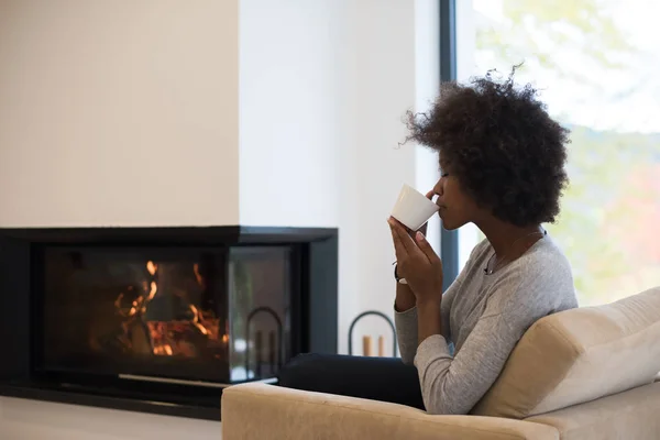 Black woman drinking coffee in front of fireplace — Stock Photo, Image