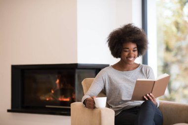 Kadın kahve içiyor ve kitap okuyor.