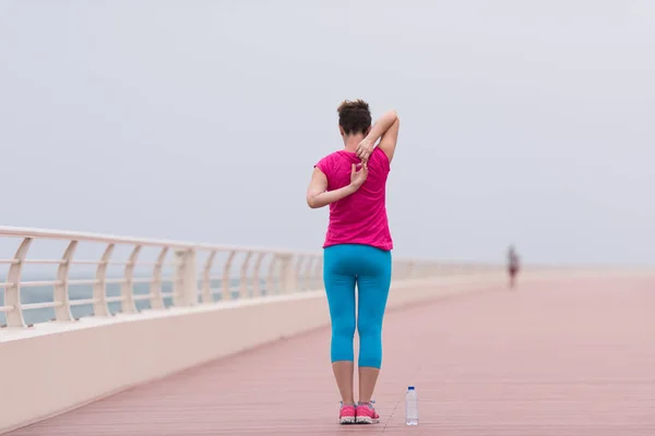 Kvinnan sträcker sig och värmer upp på strandpromenaden — Stockfoto